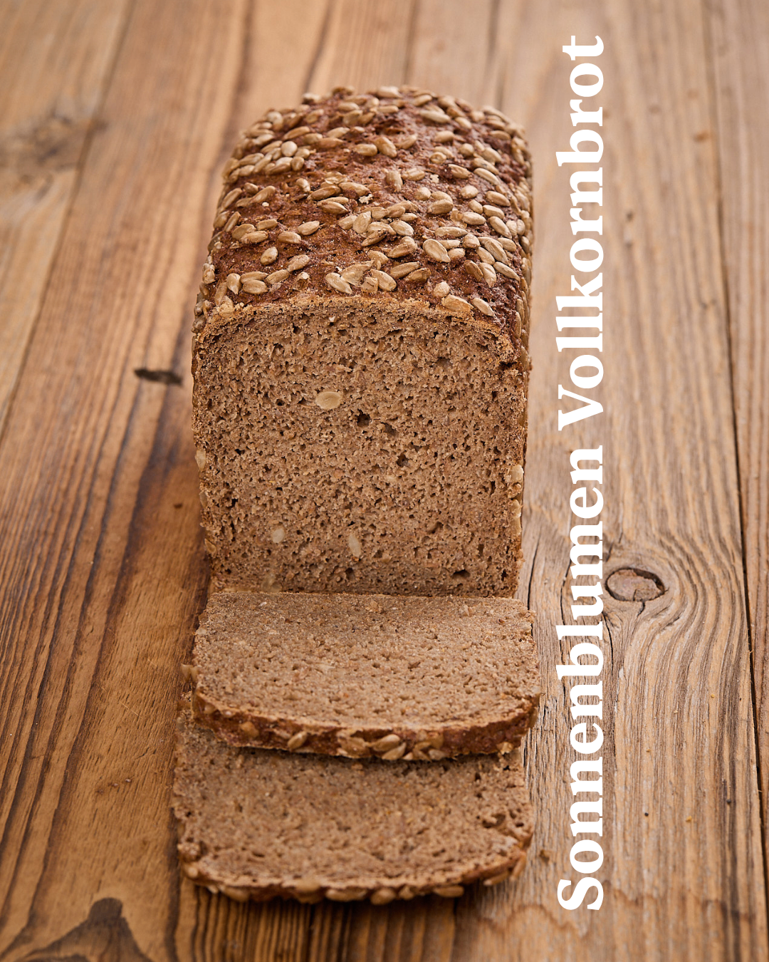 A loaf of whole grain bread with visible seeds on top, sliced into pieces on a wooden table.