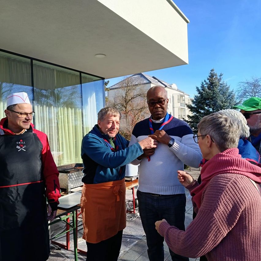 A group of people outside a building with a man in a chef's hat and another man in a white sweater holding hands.