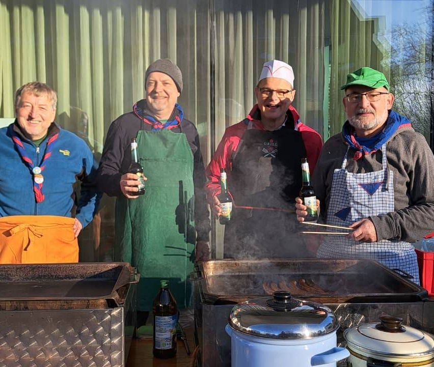 Four men stand next to each other, dressed in aprons, and holding bottles of beer. They are grilling food on a large grill with a pan. In front of the grill, there is a bottle of sauce and two pots on the table.