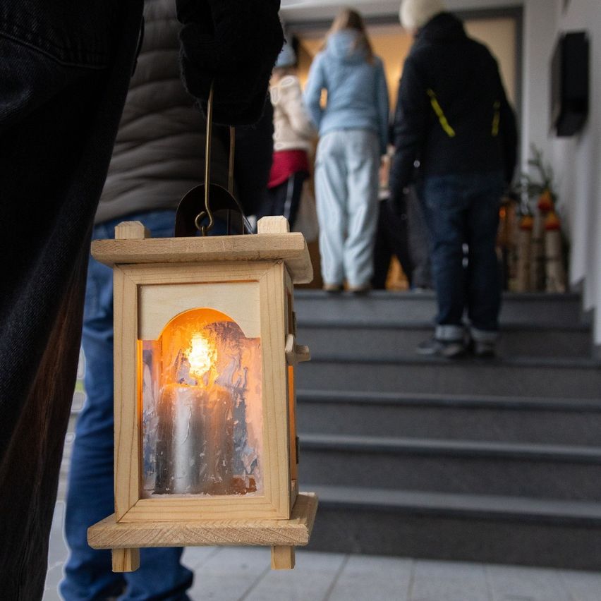 Eine Person hält eine Laterne mit einer brennenden Kerze und geht die Treppe hinauf. Andere folgen, mit einem verschwommenen Hintergrund.