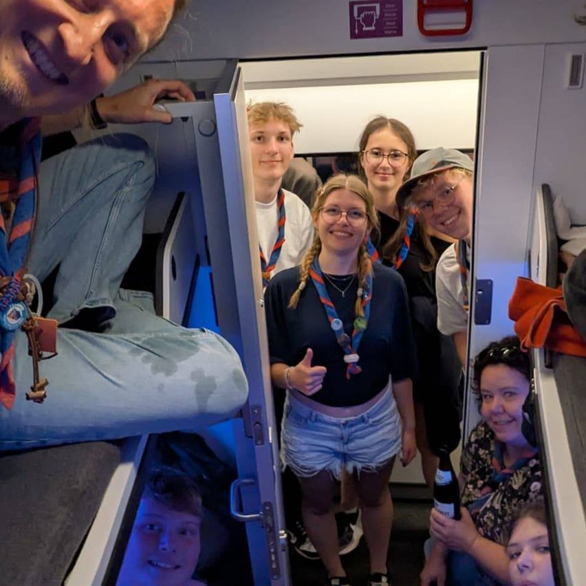 Eine Gruppe von Menschen ist in einer Kabine, einige lächeln und posieren für ein Foto. Die Kabine hat Etagenbetten und einige Leute stehen in der Nähe der Tür.