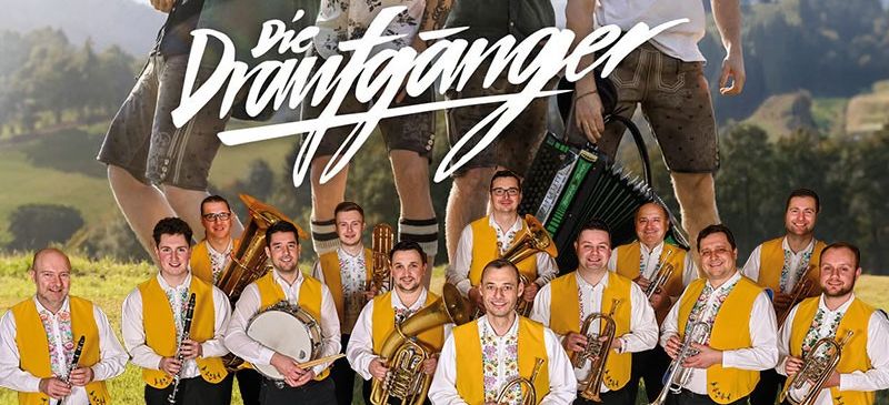 Eine Gruppe von Musikern posiert auf einer Wiese, mit einem Berg im Hintergrund. Die Gruppe lächelt und scheint für ein Foto zu posieren. Es sind mehrere Instrumente zu sehen, darunter Trompeten, ein Posaune und eine Trommel. Das Bild enthält den Text 'Die Draufganger' und 'VLADO KUMPAN und seine Musikanten'.