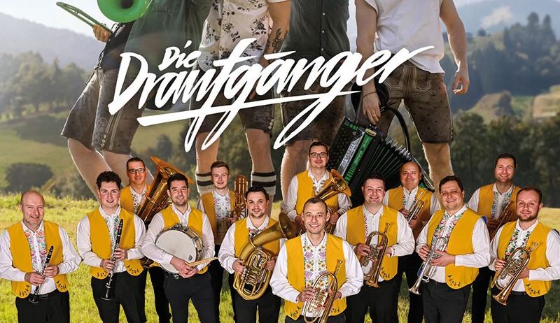 Eine Gruppe von Musikern posiert auf einer Wiese, mit einem Berg im Hintergrund. Die Gruppe lächelt und scheint für ein Foto zu posieren. Es sind mehrere Instrumente zu sehen, darunter Trompeten, ein Posaune und eine Trommel. Das Bild enthält den Text 'Die Draufganger' und 'VLADO KUMPAN und seine Musikanten'.