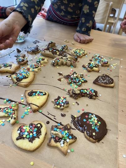 A wooden table has decorated cookies with chocolate and colorful sprinkles. Some cookies are broken.