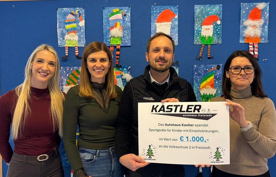 Vier Personen posieren für ein Foto mit einem Kastler-Schild, wahrscheinlich bei einer festlichen Veranstaltung. Sie stehen vor einer blauen Wand mit Weihnachtskunst. Der Mann hält ein Schild für Kastler.