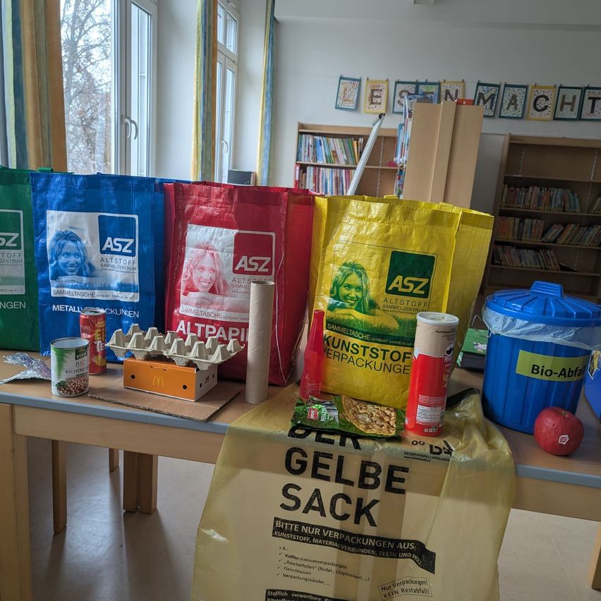 Ein Tisch mit Taschen, Dosen und anderen Gegenständen. Es gibt gelbe und blaue Taschen, eine rote Tasche und einen blauen Mülleimer. Es gibt auch Bücher in den Regalen. Es gibt einen Tisch mit einer gelben Tasche, Dosen und anderen Gegenständen. Es gibt auch Bücher in den Regalen.