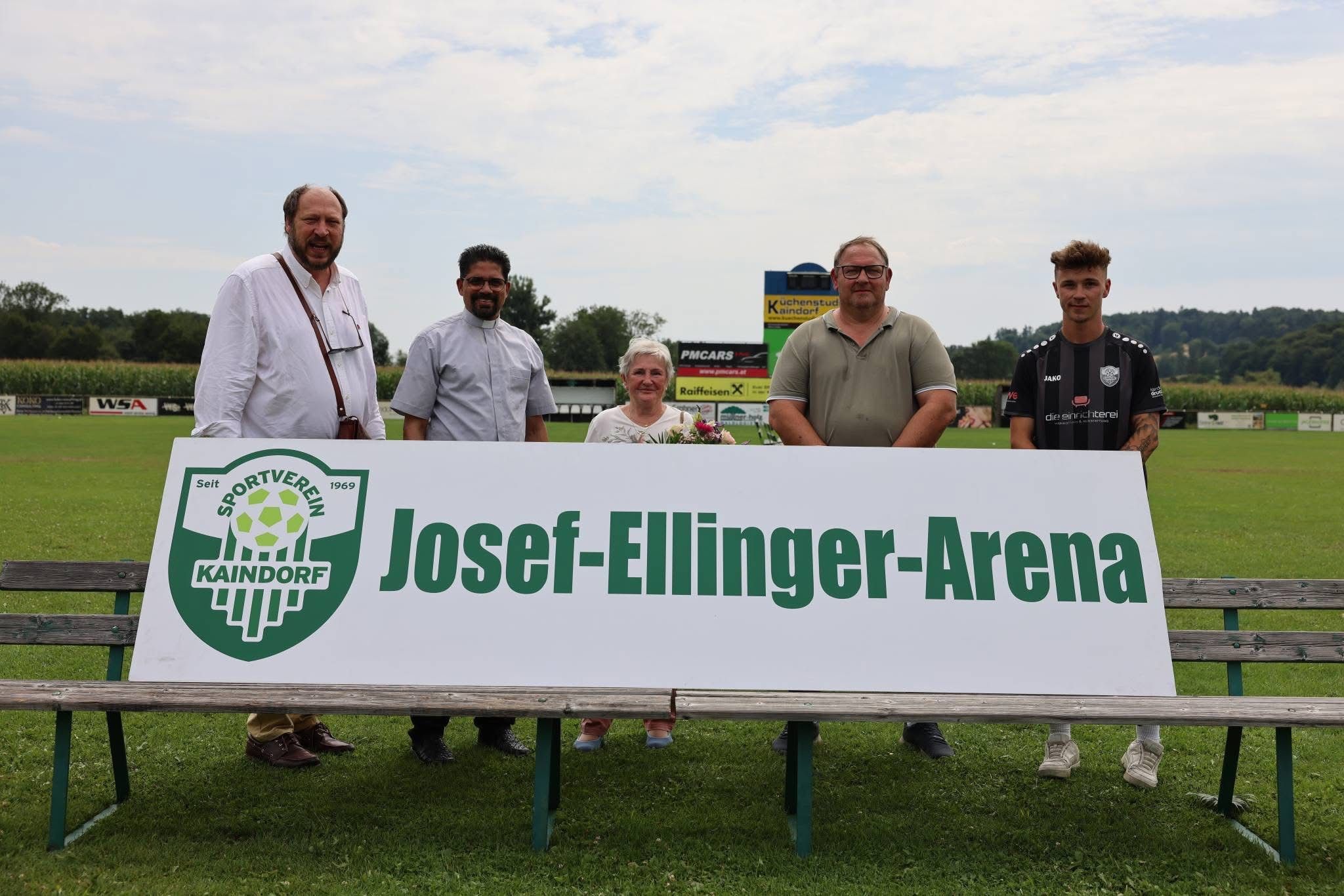 Fünf Personen stehen hinter einem großen Banner mit der Aufschrift Josef-Ellinger-Arena. Sie lächeln und scheinen für ein Foto zu posieren.