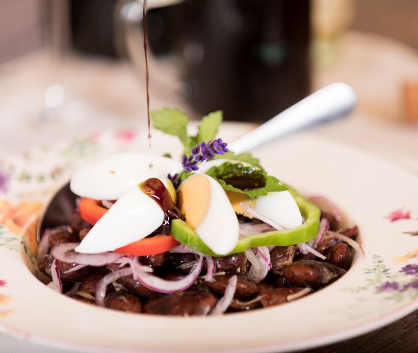 Ein Gericht aus roten Bohnen, geschnittenen weißen Eiern, roten Zwiebeln und grünem Pfeffer, garniert mit Sauce, Blumen und Kräutern, bereit zum Servieren auf einem blumigen Teller.