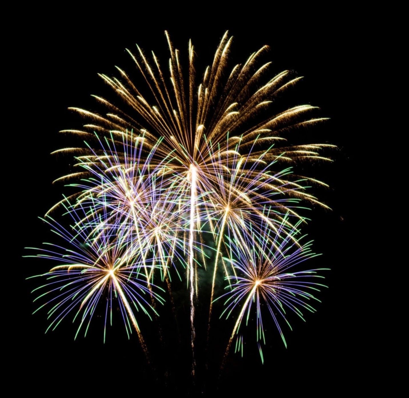 Ein nächtlicher Feuerwerksdisplay am Himmel mit mehreren farbigen Explosionen vor einem dunklen Hintergrund.