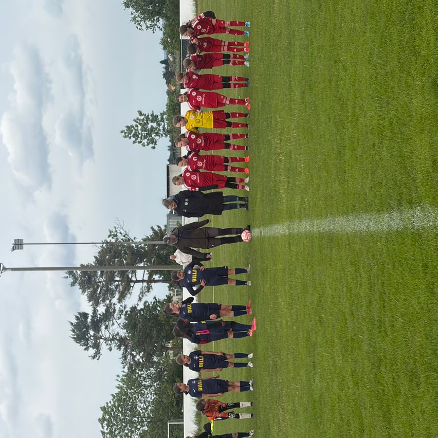 Eine Vogelperspektive von zwei Fußballmannschaften, die auf einem Feld aufgestellt sind, eine Mannschaft in Rot und die andere in Blau.