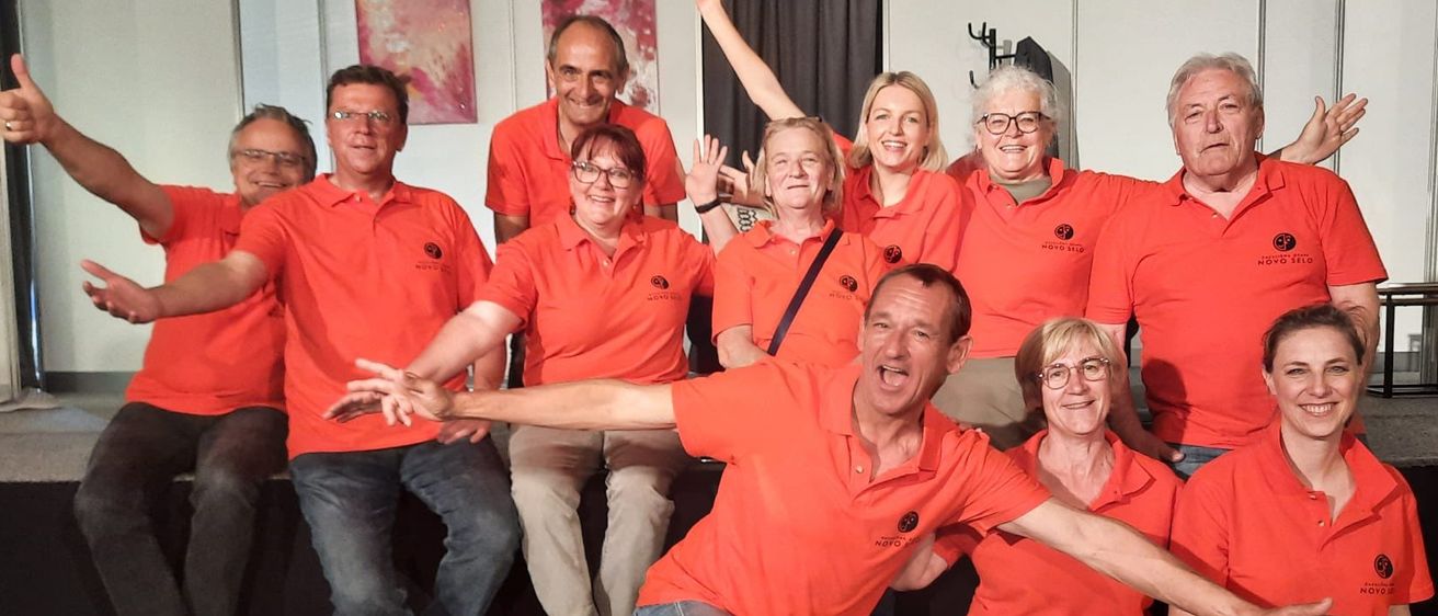 Eine Gruppe von Menschen in orangefarbenen Shirts posiert für ein Foto. Sie sitzen und stehen mit erhobenen Armen.