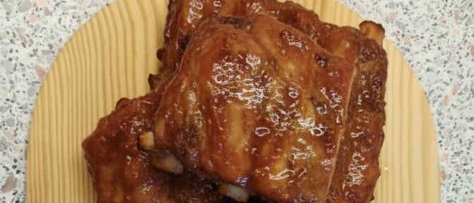 Ein hölzernes Schneidebrett hat gegrillte Rippchen, Salat und eine Schüssel mit Dressing. Die Rippchen sind mit einer Glasur gekocht.