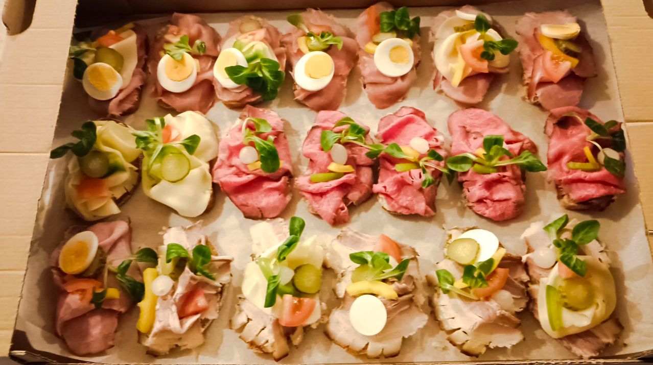 Eine Schachtel mit verschiedenen Arten von Sandwiches. Jeder Sandwich ist mit einem gekochten Ei, grünen Blättern und anderen Toppings belegt. Einige Sandwiches haben Tomatenscheiben, andere haben Gurken. Die Sandwiches sind in einer Reihe angeordnet.