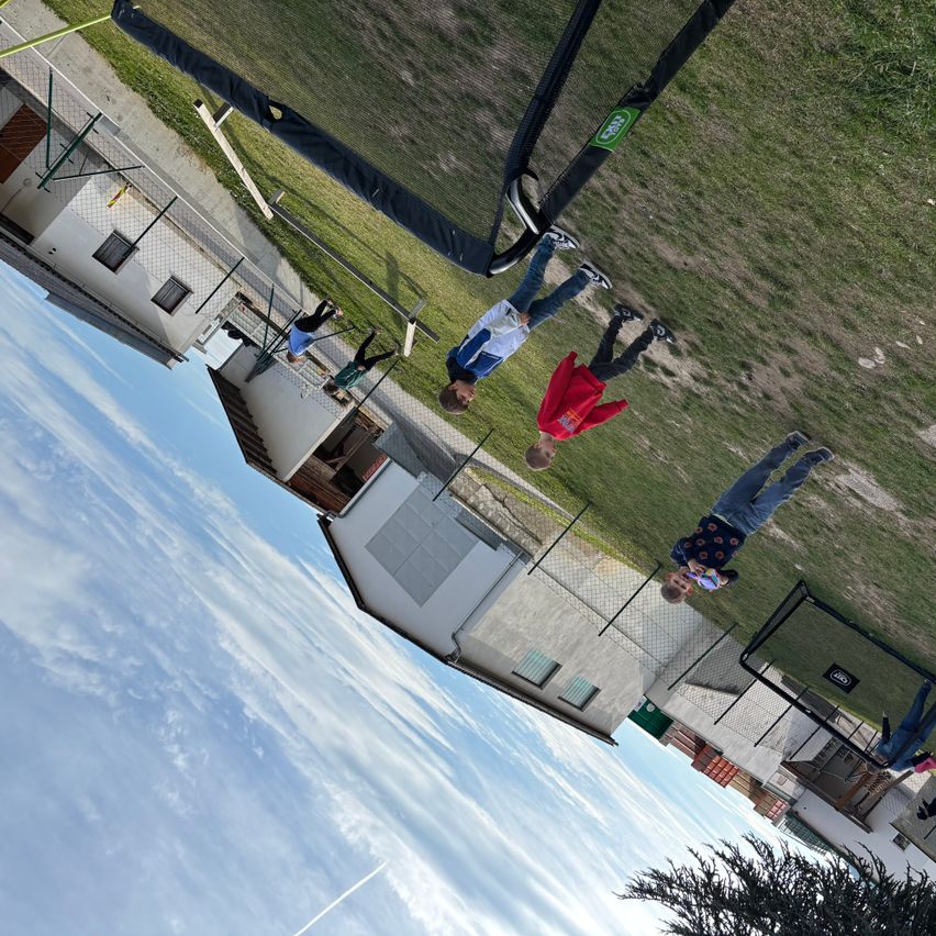 Eine Blick von oben auf mehrere Kinder, die auf einem Spielplatz spielen. Ein Kind ist auf einer Schaukel und andere sind auf dem Boden. Ein Gebäude und ein Zaun sind sichtbar.