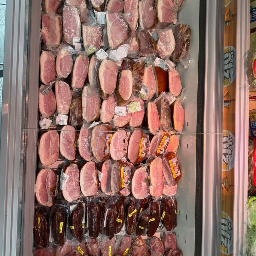 Eine Vitrine mit verschiedenen Fleischsorten in Plastikverpackungen, einschließlich Schinken, Salami und Würsten.