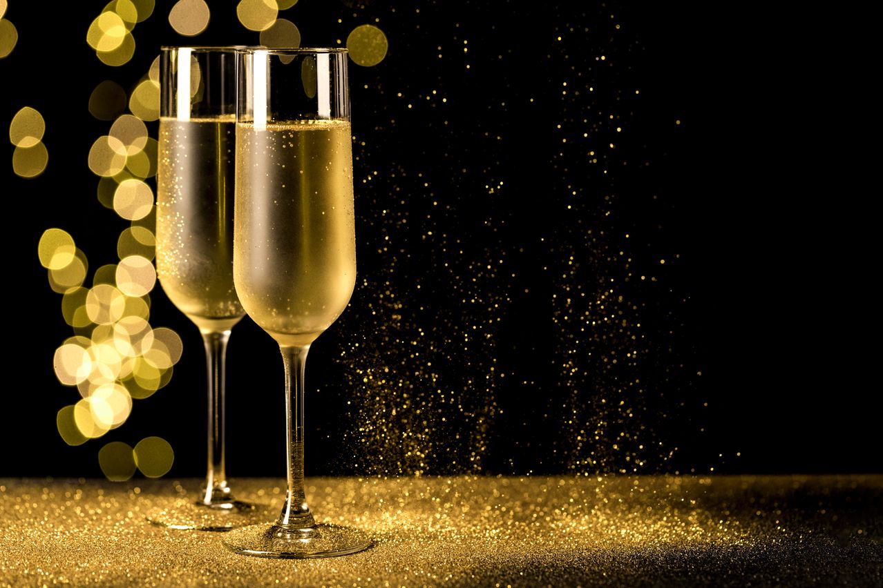 Two champagne glasses filled with sparkling champagne on a golden background with golden lights sparkling.