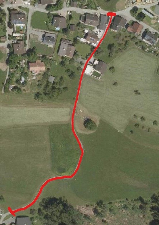 An aerial view of a rural area with houses, a field, and a winding red path.