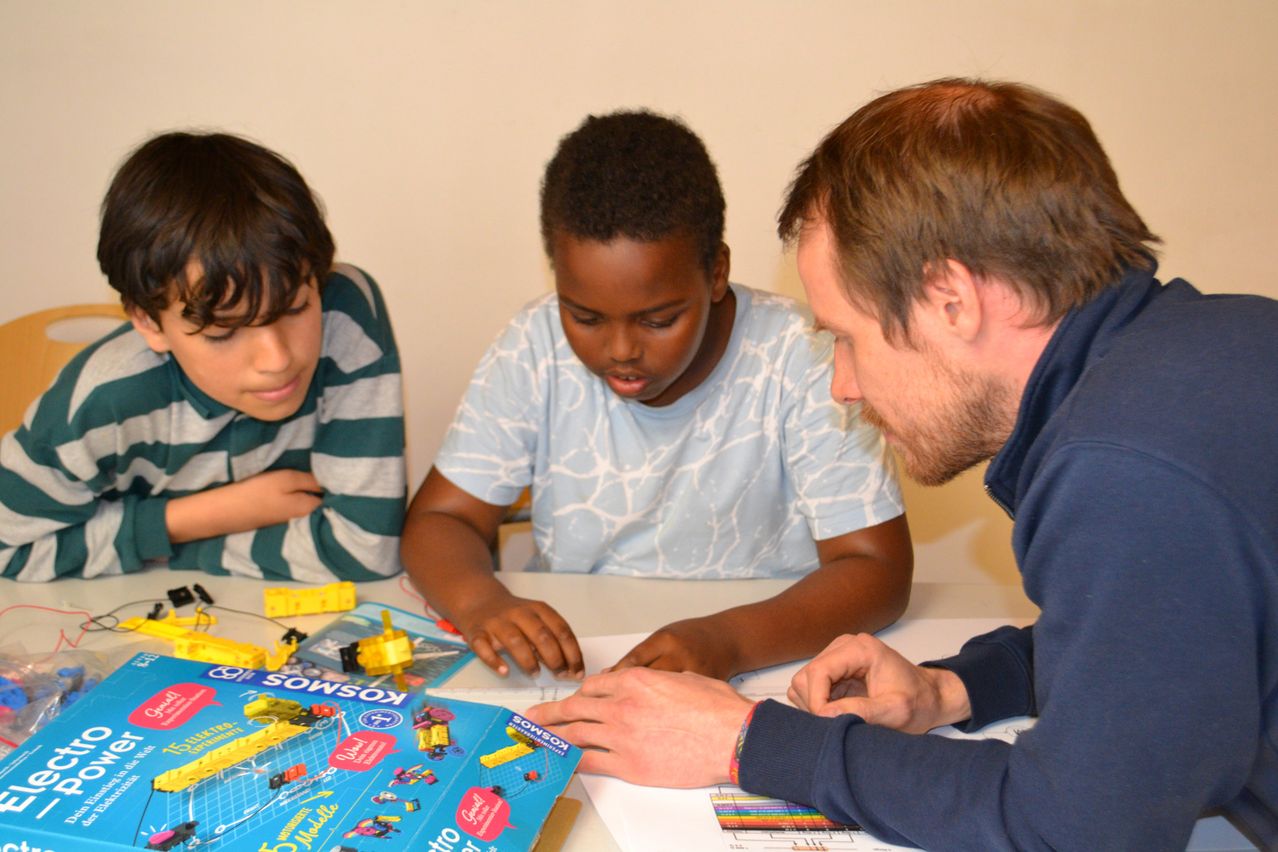 Two boys and a man are playing a board game on a table. One boy is focused on the game while the other looks on. The man is looking at the game.