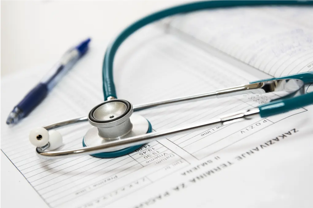 Ein Stethoskop liegt auf einem medizinischen Formular mit einem Stift in der Nähe, was auf einen Gesundheitsbereich hinweist. Das Formular enthält verschwommenen Text und Zahlen.