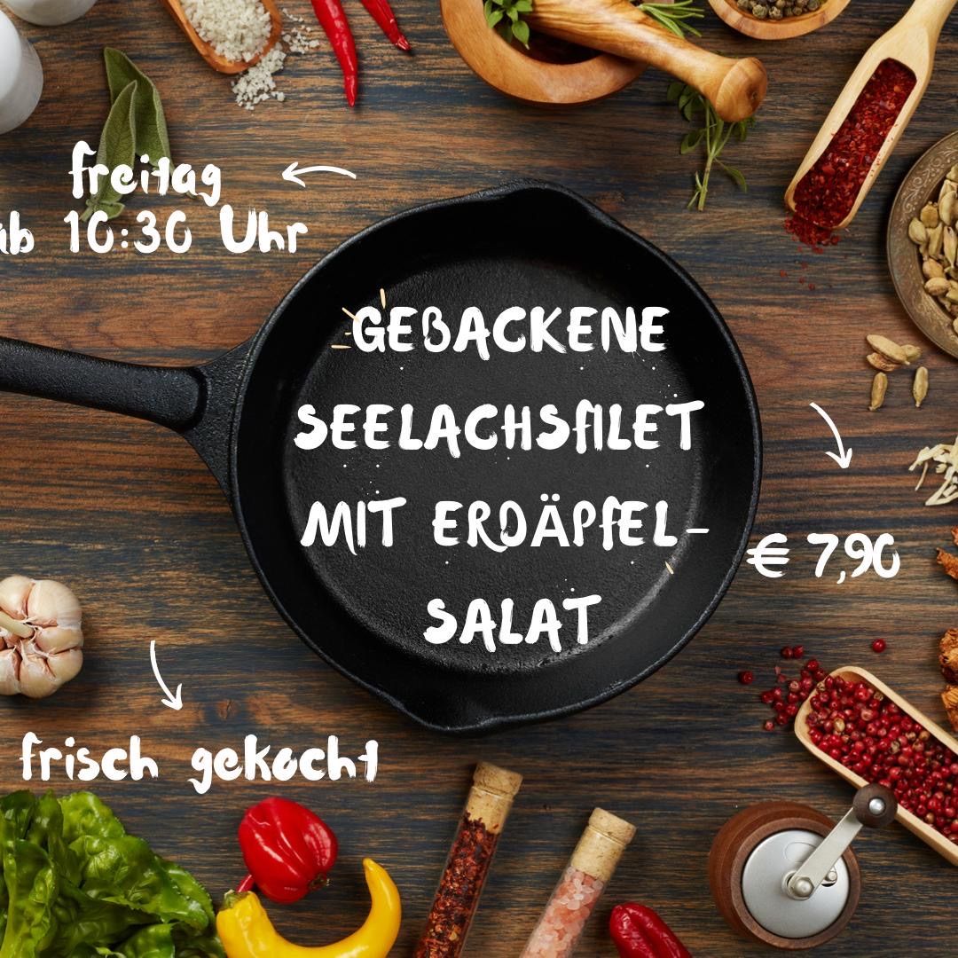 Ein Holztisch zeigt eine schwarze Bratpfanne mit Text auf Deutsch. Um die Pfanne herum befinden sich verschiedene Küchenutensilien wie Gewürze, Knoblauch und Gemüse. Der Text auf der Pfanne lautet 'Gebackene Seelachsfilet mit Erdapfelsalat' und '€ 7,90'. Das Bild ist gut komponiert mit einem rustikalen Look.