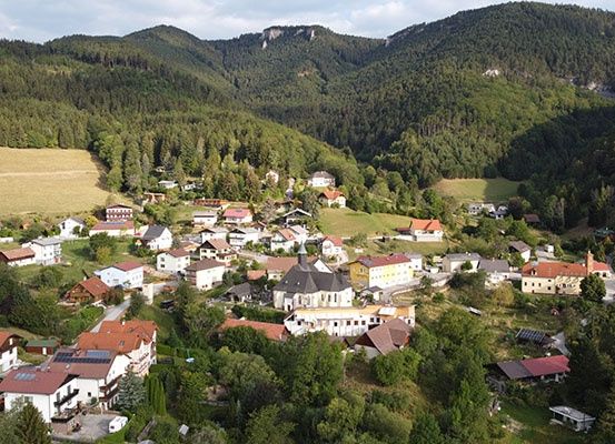 Ein Dorf mit vielen Häusern und Gebäuden, umgeben von Bäumen und Bergen. Das Dorf liegt in einem Tal.
