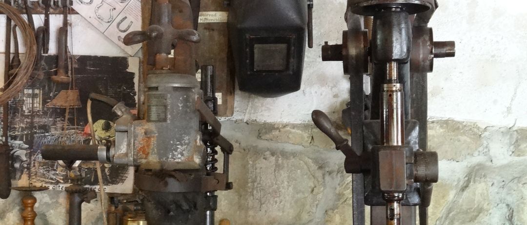 Eine Werkstatt mit verschiedenen alten Maschinen und Werkzeugen, einschließlich einer Bohrmaschine und einer Schweißmaske, an einer Steinwand montiert.