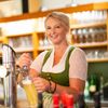 Eine Frau in einem grünen Kleid lächelt, während sie ein Glas Bier aus einem Zapfhahn in einer Bar einschenkt.
