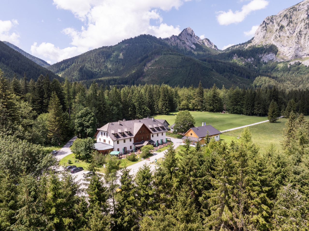 Eine Luftaufnahme eines rustikalen Berghotels in einem üppig grünen Tal, umgeben von hohen Bergen.
