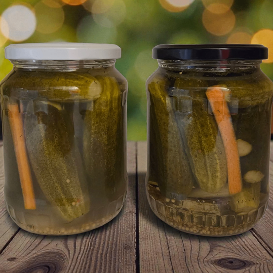 Zwei Glasgläser mit eingelegten Gurken und Karotten stehen auf einem Holztisch. Die Gläser haben Deckel, eines weiß und eines schwarz.