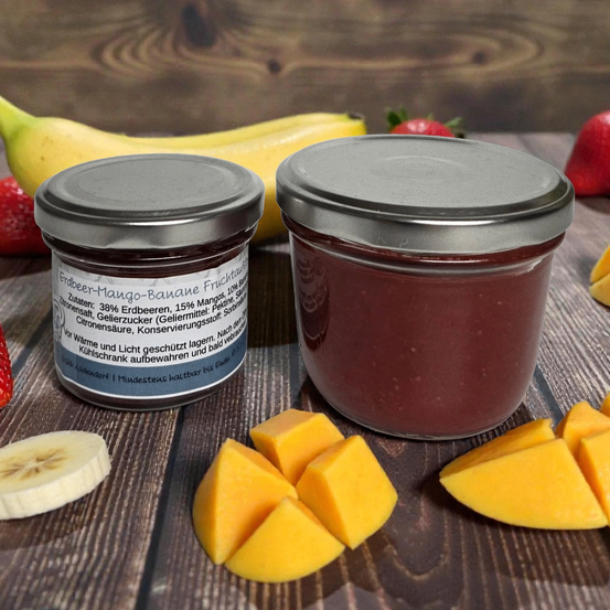 Zwei Gläser mit Erdbeer-Mango-Bananen-Fruchtaufstrich mit geschnittenen Mangos und Bananen auf einer Holzoberfläche.