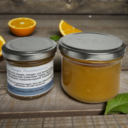 Zwei Glasgläser mit silbernen Deckeln, die einen Fruchtaufstrich enthalten, stehen auf einer Holzoberfläche. Orangenscheiben und Minzblätter sind im Hintergrund zu sehen. Die Glasetiketten zeigen an, dass es sich um Orangenfruchtaufstrich handelt.