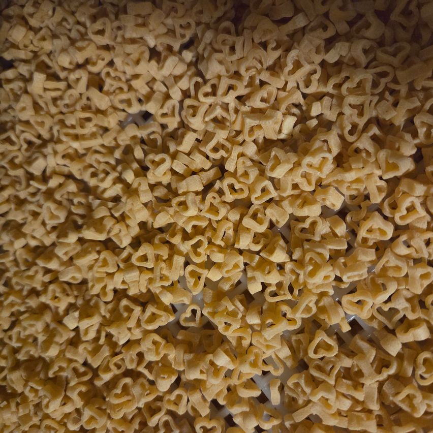 Eine Nahaufnahme eines großen Haufens herzförmiger Nudeln, ordentlich auf einer weißen Oberfläche angeordnet.