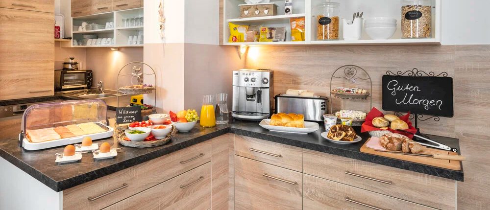Eine moderne Küche mit Holzschränken, einem Frühstücksbuffet mit Brot, Eiern und Obst, einer Kaffeemaschine und einem Toaster auf der Arbeitsplatte.