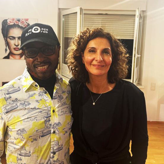 Ein Mann und eine Frau stehen zusammen und lächeln für ein Foto vor einer Wand mit einem Bild einer Frau.