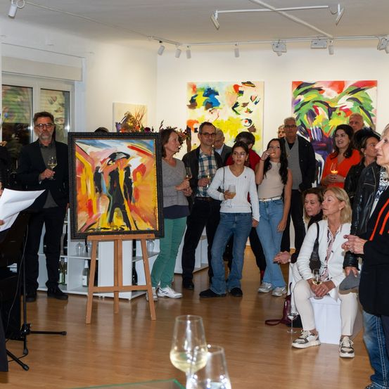 Eine Kunstgalerie-Veranstaltung mit Menschen, die bunte Gemälde bewundern, ein zentrales Gemälde auf einem Staffelei, Weinglas in der Hand und lebhafte Unterhaltung.