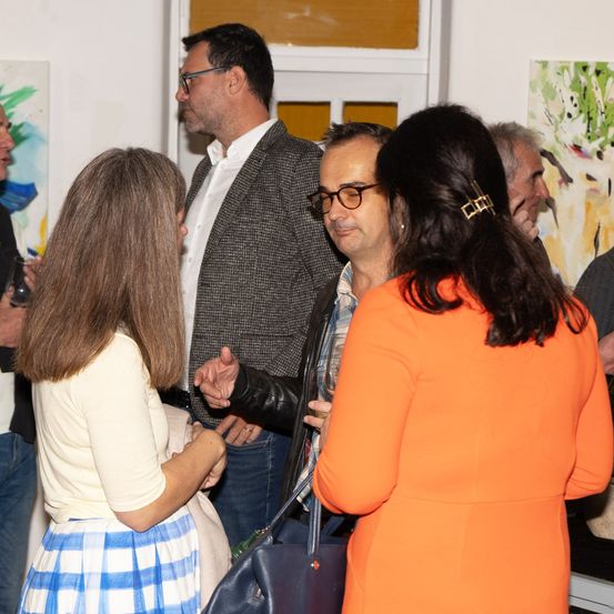 Eine Gruppe von Menschen, darunter zwei Männer und zwei Frauen, steht in einer Kunstgalerie und diskutiert scheinbar über Kunstwerke.