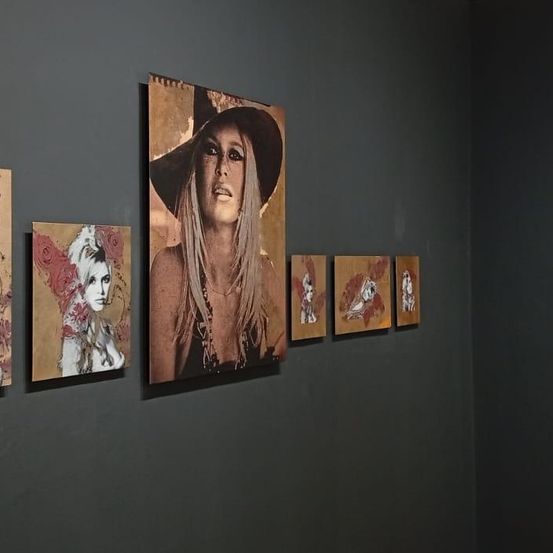 An einer Wand sind sechs Kunstwerke ausgestellt, darunter ein prominentes Porträt einer Frau mit Hut, umgeben von kleineren Porträts mit abstrakten Stilen und Rosenmotiven.