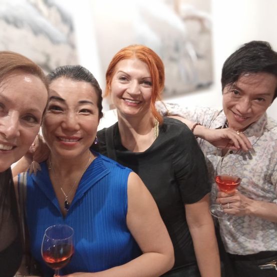 Vier Menschen posieren lächelnd für ein Foto in einer Kunstgalerie. Die Frau in Blau hält ein Weinglas. Hinter ihnen sind große, abstrakte Gemälde.