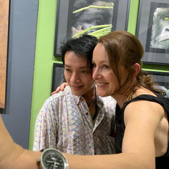 Zwei Frauen lächeln und posieren für ein Selfie vor einer grünen Wand mit Tiergemälden.