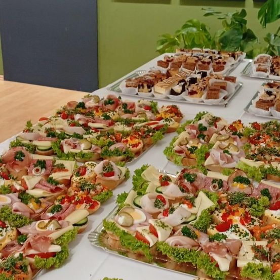 Eine Auswahl an Sandwiches und Gebäck wird in einem Speisebereich auf Tabletts präsentiert. Die Sandwiches sind mit Fleisch, Gemüse und Käse belegt.