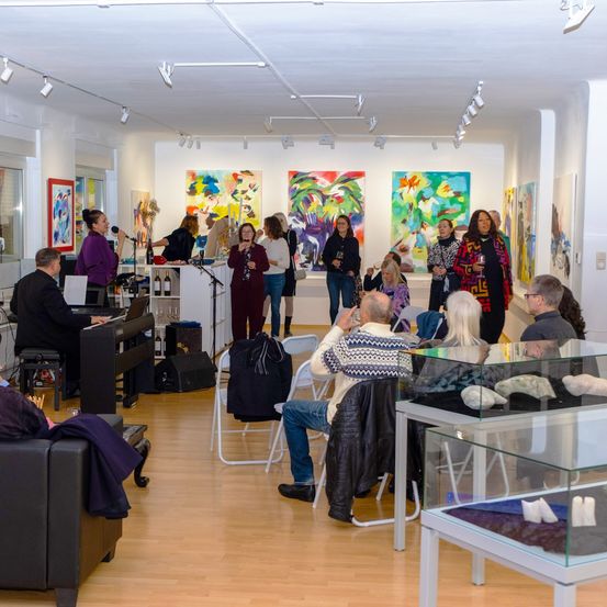 Eine Gruppe von Menschen befindet sich in einer Kunstgalerie, einige sitzen und andere stehen. Ein Pianist spielt in der Ecke. Mehrere Gemälde hängen an den Wänden.