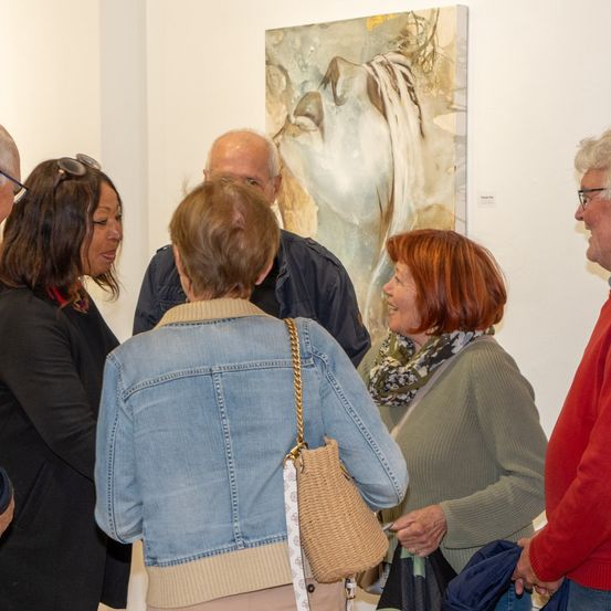 Eine Gruppe von Menschen steht vor einem Gemälde in einer Kunstgalerie und diskutiert dessen Merkmale.