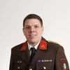 Ein Mann in Uniform lächelt in die Kamera. Die Uniform besteht aus Schulterklappen, Abzeichen und Medaillen. Der Name 'Sebersdorf' ist auf der rechten Brustseite gestickt.