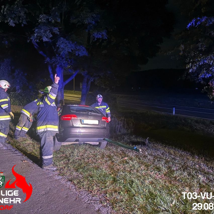 Feuerwehrleute in Schutzausrüstung helfen einem Auto, das nachts von der Straße abgekommen ist. Das Auto steht auf dem Rasen neben der Straße, und die Feuerwehrleute verwenden ein Seil, um es zu sichern.