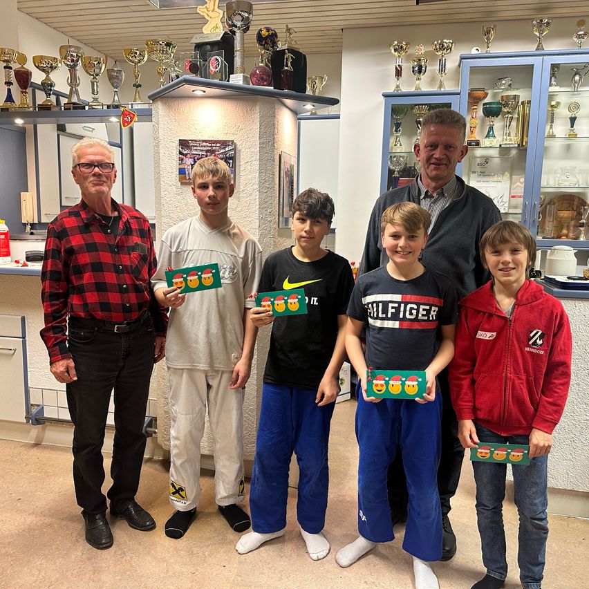 Eine Gruppe junger Jungen mit Zertifikaten und Erwachsenen in einem Raum mit Trophäen und Auszeichnungen zur Ausstellung.