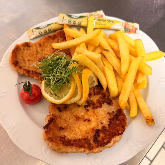 Ein Teller mit zwei panierten Fleischstücken, Pommes Frites und einer Kirschtomate mit Kräutern.