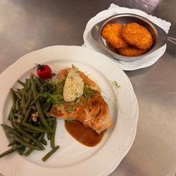 Ein Teller mit Lachs, grünen Bohnen und einer Beilage aus gebratenen Kartoffelbällchen.