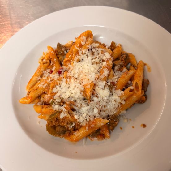Auf einem weißen Teller liegt Pasta mit Tomatensoße, überzogen mit geriebenen Käse und Hackfleisch.