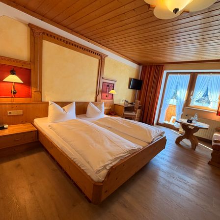 Ein gemütliches Hotelzimmer mit einem Doppelbett, Holzmöbeln und Blick auf das Freie.