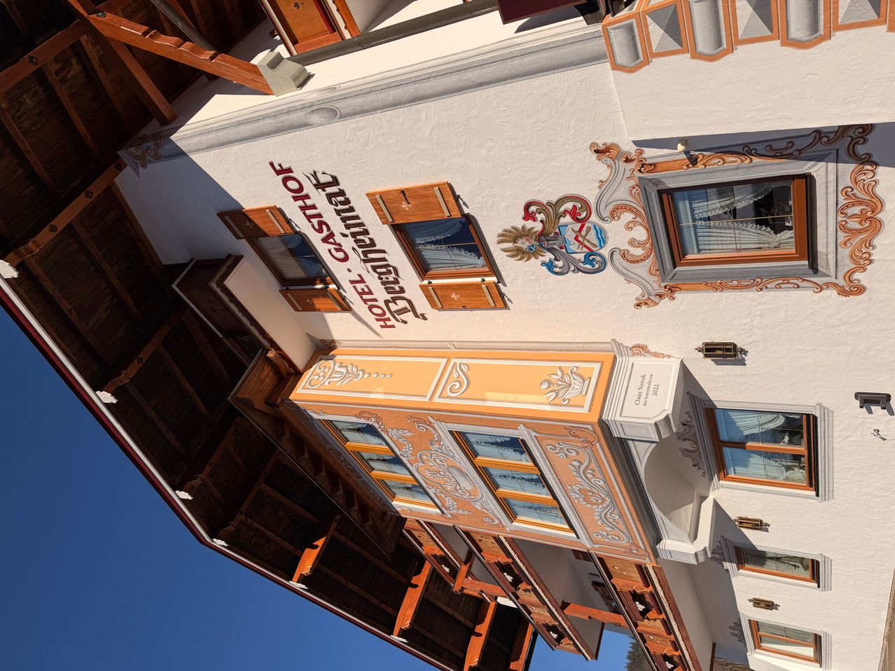 A top-down view of a white and orange building. It has a design above the windows and a name on the wall. The windows are closed.